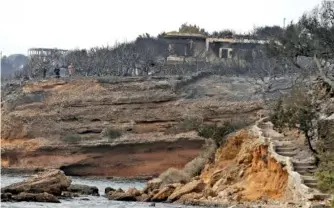  ?? AP FILE PHOTO BY THANASSIS STAVRAKIS ?? Firefighte­rs stand on a cliff top where burned trees hug the coastline in Mati east of Athens in July after wildfires raged through the popular seaside areas near the Greek capital.