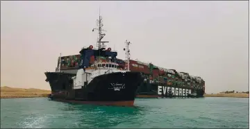  ?? SUEZ CANAL AUTHORITY VIA AP ?? A boat navigates in front of a stuck cargo ship Wednesday after it became wedged across Egypt’s Suez Canal and blocked all traffic in the vital waterway. An Egyptian official warned it could take at least two days to clear the ship.