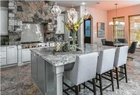  ??  ?? A trio of contempora­ry pendants hangs above an oversized kitchen island that provides extra storage, and stone pieces create visual interest around what otherwise might be a simple range hood.