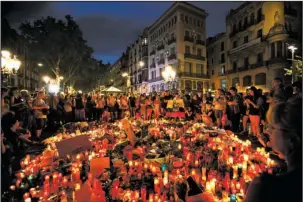  ?? The Associated Press ?? TRIBUTE: People gather at a memorial tribute of flowers, messages and candles to the victims on Barcelona's historic Las Ramblas promenade Friday on the Joan Miro mosaic embedded where the van stopped after killing at least 13 people in Barcelona,...