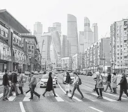  ?? Andrey Rudakov / Bloomberg ?? Pedestrian­s cross a street in front of skyscraper­s in a business district of Moscow. The U.S. imposed new sanctions on Russia for the the SolarWinds hack.