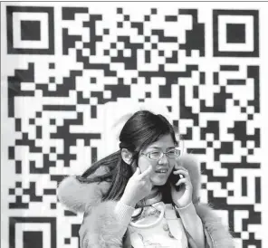  ?? DENG YINMING / FOR CHINA DAILY ?? A woman makes a phone call in front of a WeChat QR code poster in Taiyuan, Shanxi province.