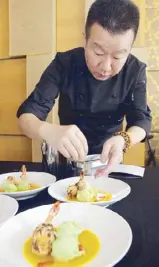  ??  ?? Chef Jereme Leung puts finishing touches to the crispy black rice-coated king prawn in pumpkin sauce.