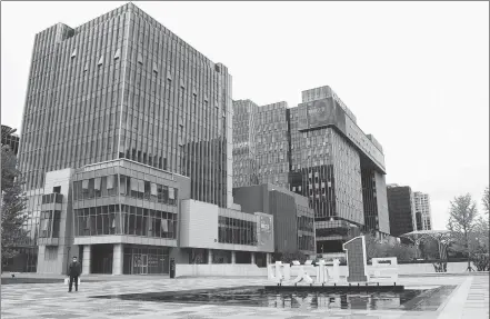  ?? REN CHAO / XINHUA ?? A pedestrian walks past a building in Zhongguanc­un No 1, an office building cluster, in Beijing.