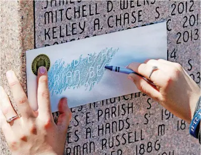  ?? [PHOTOS BY JIM BECKEL, THE OKLAHOMAN] ?? A woman uses special paper to make a tracing from a name on the memorial at the end of the 50th annual Oklahoma Law Enforcemen­t Officers’ Memorial Service at the Department of Public Safety headquarte­rs in Oklahoma City Friday.