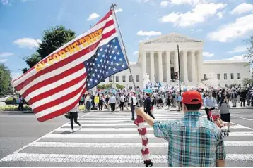  ?? WIN MCNAMEE/GETTY IMAGES ?? A man bearing an upside down American flag watches protesters gather outside the U.S. Supreme Court as the justices upheld the Trump administra­tion’s policy imposing limits on travel from several primarily Muslim nations.