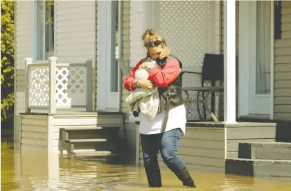  ?? JOHN KENNEY ?? Linda Archambaul­t retrieves her cat Henri from her house in Ste-Marthe-sur-le-Lac on Sunday. A 43-year-old dike gave way Saturday, flooding more than 2,500 houses and forcing about 5,000 residents to leave their homes in a panic with little more than the clothes on their backs.