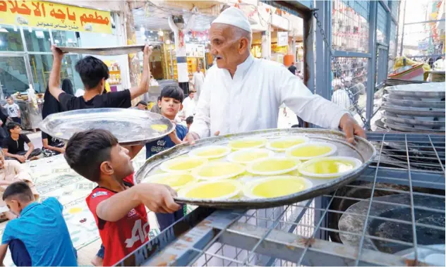  ?? Reuters ?? ↑
Iraqi Muslims carry plates as people gather to break their fast in Najaf on Sunday.