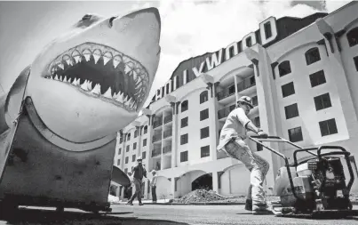  ?? THE COMMERCIAL APPEAL ?? A Hollywood Casino constructi­on worker pulls a compactor along freshly laid asphalt outside the casino under the watchful eye of the 22-foot Fiberglass shark from the movie “Jaws” on July 27, 1994, in Tunica. The 600-pound fish, used in close-ups during filming of the movies, was later moved inside the casino and hung from the ceiling over one of the bars.