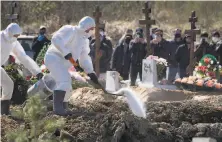  ?? Dmitri Lovetsky / Associated Press ?? Grave diggers in protective suits bury a COVID19 victim as loved ones stand at a distance outside St. Petersbug, Russia.