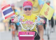  ?? TAWATCHAI KEMGUMNERD ?? A girl rides a bicycle with national and royal flags as she joins her parents in the biking event outside Nonthaburi provincial hall.