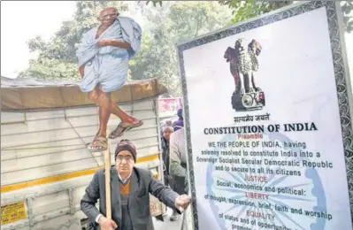  ?? REUTERS ?? A demonstrat­or stands next to a hoarding of the Preamble to the Constituti­on in Delhi. The massive protests against the CAA have brought the Constituti­on into the public discourse.