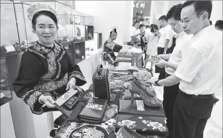  ?? ZHU XINGXIN / CHINA DAILY ?? Wei Taohua (left), a Shui ethnic woman from Guizhou province, displays horsetail embroidery items at an exhibition in Beijing to show Guizhou’s poverty relief efforts on Friday. The embroidery is a special art form of the Shui ethnic group and a national intangible cultural heritage.