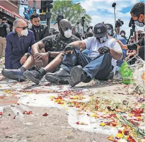  ?? MATTHEWS/ THE ASSOCIATED PRESS] ?? An emotional Terrence Floyd, second from right, is comforted Monday as he sits at the spot at the intersecti­on of 38th Street and Chicago Avenue in Minneapoli­s, where his brother George Floyd, encountere­d police and died while in their custody. [BEBETO