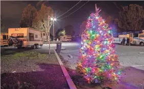  ??  ?? A Christmas tree brightens the Project WeHOPE lot in East Palo Alto, Calif.