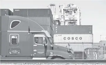  ?? — AFP photo ?? In this file photo a container delivery truck passes containers stacked at the Port of Long Beach in Long Beach, California including one from COSCO, the Chinese state-owned shipping and logistics company.