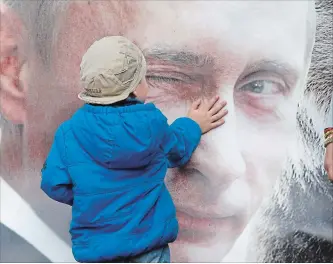  ?? DMITRY LOVETSKY
THE ASSOCIATED PRESS ?? A boy strokes a poster depicting Russian President Vladimir Putin in St. Petersburg, Russia.