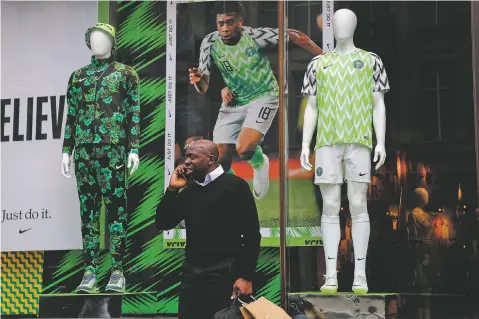  ?? FRANK AUGSTEIN/ASSOCIATED PRESS ?? A man stands in front of a Nigerian national soccer team jersey on display June 5 at a shop in London. With just days to go before the FIFA World Cup, some winners and losers have emerged among the often wild and wacky team jerseys.