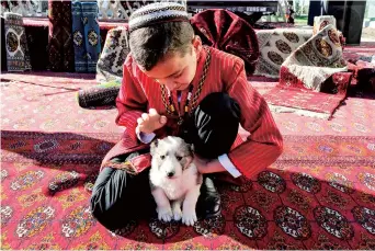  ??  ?? A Turkmen boy wearing a traditiona­l dress caresses an alabai shepherd dog puppy at a kennel outside Ashgabat. — AFP