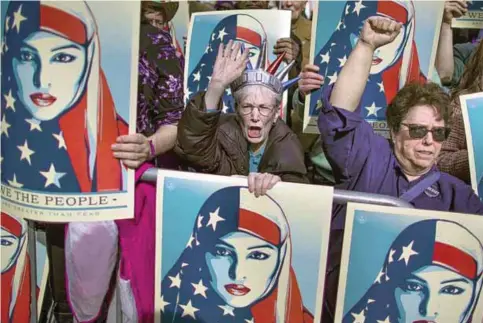  ??  ?? NEW YORK: In this file photo, people carry posters during a rally against President Donald Trump’s executive order banning travel from seven Muslim-majority nations, in New York’s Times Square. —AP