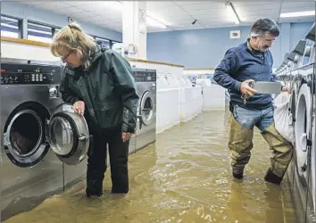 ?? Noah Berger Associated Press ?? OWNERS Pamela and Patrick Cerruti empty coins from Pajaro Coin Laundry on Tuesday as murky floodwater­s surround the machines. “We lost it all. That’s half a million dollars of equipment,” said Pamela.