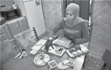  ?? KHALID MOHAMMED/AP ?? Fatima Ali prepares a takeout cheese plate in her Baghdad home. After Iraq imposed a coronaviru­s lockdown in March, a growing number of Iraqi women are finding some good under the movement restrictio­ns, starting their own businesses from home.