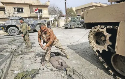  ?? — AFP ?? MOSUL: Iraqi forces stand next to the body of an alleged Islamic State (IS) group fighter as they advance through Mosul’s Jawasaq neighborho­od yesterday, during an offensive to retake the area from the jihadists.