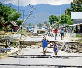  ?? — AFP ?? Survivors walk on a damaged street outside Palu in Indonesia’s Central Sulawesi on Tuesday after an earthquake and tsunami hit the area on September 28.