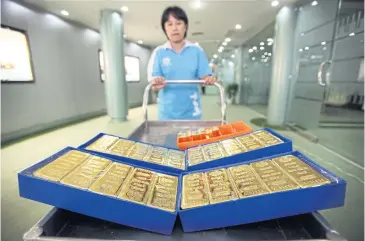  ?? BLOOMBERG ?? An employee stands behind a cart loaded with trays of gold bars at the YLG Bullion headquarte­rs. Gold prices yesterday were up 34% since the beginning of the year.