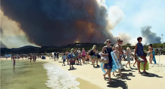  ?? (Afp Photo/Poujoulat) ?? Via dalla spiaggia I bagnanti abbandonan­o la spiaggia mentre alle loro spalle bruciano le colline attorno a Bormes-les-Mimosas, il «villaggio più fiorito della Francia»