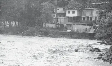  ??  ?? People walk near Tiribi river flooded by heavy rains of Tropical Storm Nate that affects the country in San Jose, Costa Rica. — Reuters photo