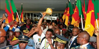  ??  ?? THE HEROES ARE BACK IN TOWN . . . Captain Benjamin Moukandjou ( ABOVE) proudly holds the Nations Cup trophy as he makes his way past an excited crowd on arrival back in Yaounde this week while forward Christian Bassogog ( RIGHT), who was named the best...