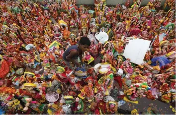  ?? — AP ?? An boy searches for reusable items amid idols of Goddess Dashama and worship materials lying on the bank of the Sabarmati river at the end of Dashama festival in Ahmedabad on Tuesday.