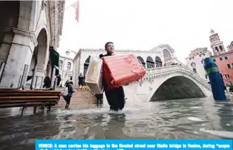  ??  ?? VENICE: A man carries his luggage in the flooded street near Rialto bridge in Venice, during “acqua alta”, or high water, of 160 centimeter­s. —AFP