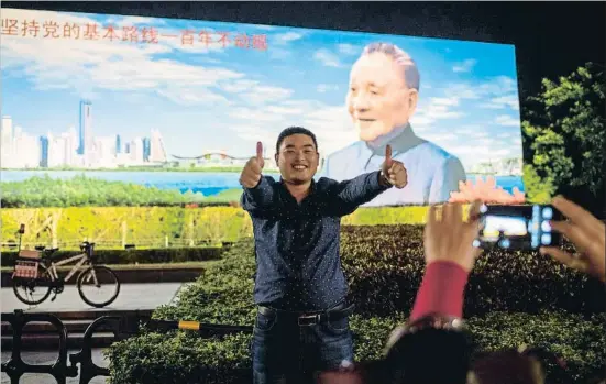  ?? NICOLAS ASFOURI / AFP ?? Un hombre posa para una fotografía delante de un gran cartel con una imagen de Deng Xiaoping en Shenzhen