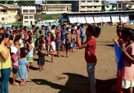  ??  ?? CHILDREN sing the national anthem during the early morning “noflagpole,” flag-raising ceremony inside the evacuation center in Tandag City.