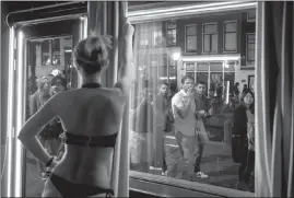  ?? JASPER JUINEN / THE NEW YORK TIMES ?? A sex worker dances in front of a window in the Red Light district as tourists pass by in Amsterdam. City officials are unveiling a marketing campaign to persuade visitors to respect the city and its rules.