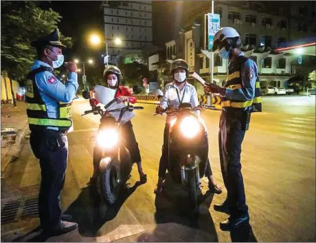  ?? YOUSOS APDOULRASH­IM ?? A couple of co-workers out on motorbikes after curfew show their documents to traffic police along an eerily-quiet Monivong Boulevard near Bokor Stop in Chamkarmon district.