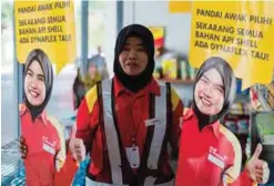  ??  ?? BENTONG, Malaysia: A Shell petrol station employee holds up life-sized cutouts depicting a female staff member, pictured in uniform with a black Muslim headscarf and placed beside individual self-serve petrol pumps as part of a promotiona­l campaign, as...