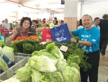  ??  ?? Chan (right) distribute­s a reusable shopping bag to one of the vegetable sellers at Stutong Community Market.