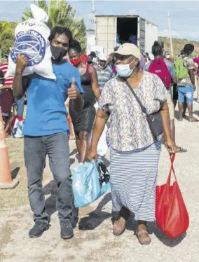  ??  ?? An elderly woman is assisted with her three bags of food and personal care items that she received from New Fortress Energy Foundation in partnershi­p with Food For the Poor and the Ministry of Labour and Social Security.