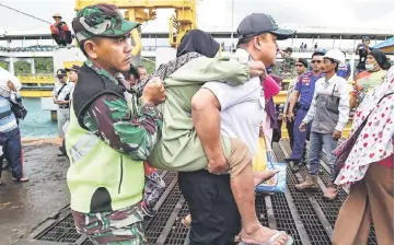  ??  ?? Members of an Indonesian search and rescue team assist an elderly woman (centre) as she disembarks from a ferry at the port after being evacuated from Sebesi Island, in Bakauheni in Lampung province. — AFP photo