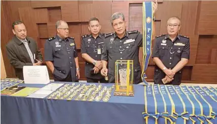  ?? PIC BY SHARUL HAFIZ ZAM ?? Kedah police chief Datuk Asri Yusoff (second from right) with sashes, medals and souvenir trophies seized from the organiser.