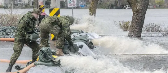  ?? DAVE SIDAWAY ?? Firefighte­rs and military personnel reinforce 1.2 kilometres of makeshift dikes along Lalande Blvd. in Pierrefond­s on Wednesday in an attempt to keep the flooding at bay.