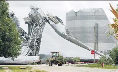  ?? THE ASSOCIATED PRESS ?? Iowa Department of Transporta­tion workers help with tree debris removal as grain bins from the Archer Daniels Midland facility are seen severely damaged in Keystone, Iowa, on Aug. 12. A storm slammed the Midwest with straight line winds of up to 100miles per hour on Monday, gaining strength as it plowed through Iowa farm fields, flattening corn and bursting grain bins still filled with tens of millions of bushels of last year’s harvest.