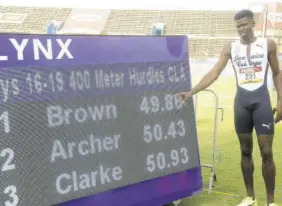  ??  ?? Javier Brown of Jamaica College poses beside the display board which highlights his record 49.86 seconds win in the 400m hurdles Open yesterday.