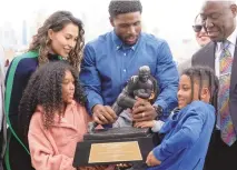  ?? ASSOCIATED PRESS ?? Former USC football player Reggie Bush with his family try to lift the Heisman Trophy for a photo during a news conference at the Los Angeles Memorial Coliseum on Thursday.