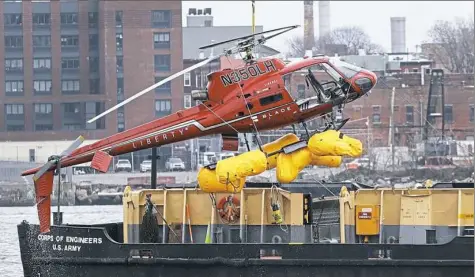  ?? Associated Press ?? A helicopter is hoisted by crane from the East River onto a barge Monday in New York. The pilot was able to escape the Sunday night crash after the aircraft flipped upside down in the water killing five passengers, officials said.