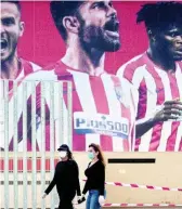  ?? AP ?? Two women wearing face masks pass by a giant poster of Atlético Madrid players at the Wanda Metropolit­ano stadium in Madrid, Spain.