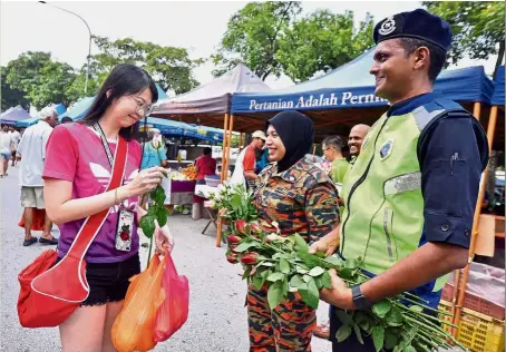  ??  ?? Police and fire department personnel from Subang Jaya, Selangor, joined members of the Zone 3 Residents’ Committee to hand out roses to market-goers in USJ Taipan on Sunday. — RAJA FAISAL HISHAN/ The Star
